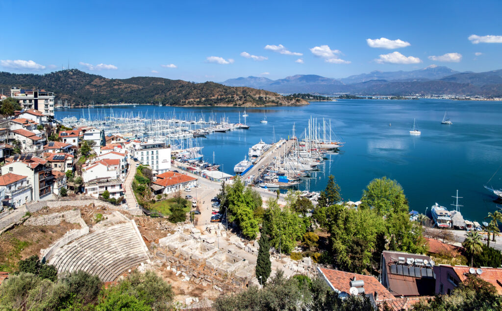 Fethiye harbor with yachts and boats and mountains. There are ruins of Ancient Theater Antik Tiyatrosu on foreground. Mugla Province.